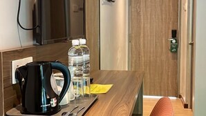 A hotel room with a wooden desk, a black coffee maker, two water bottles, and a pair of scissors. - White Lodge (Langkawi)