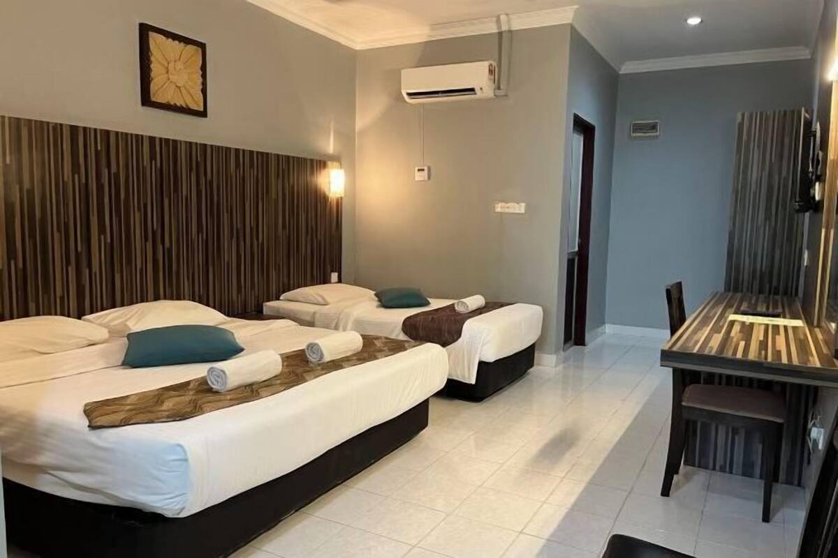 A hotel room with three beds, a dining table, and an air conditioning unit.