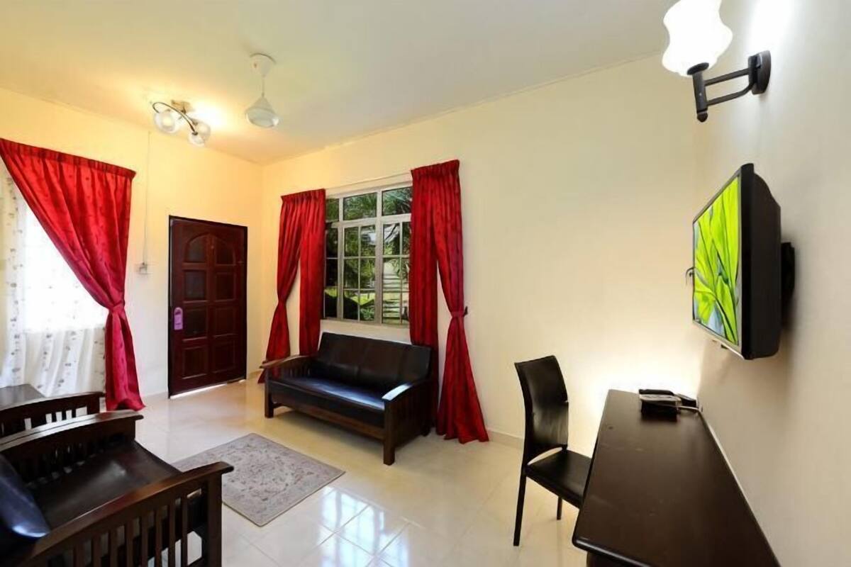A living room with a sofa, a coffee table, a TV mounted on the wall, and a door with red curtains.