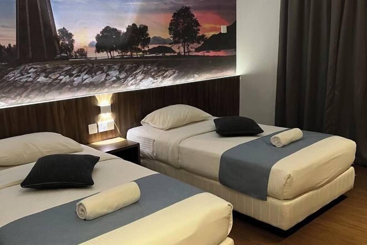 A hotel room with two beds, each with a pillow and a rolled towel. There is a painting above the beds depicting a landscape.