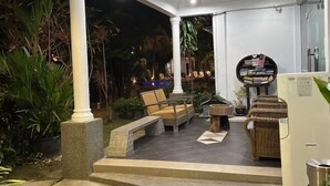 A covered outdoor seating area with a stone bench, a round table, and a wicker chair. - White Lodge (Langkawi)