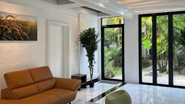 A modern interior with a sofa, a potted plant, and a large glass door leading to a garden. - White Lodge (Langkawi)