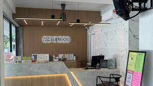 A reception area with a wooden panel wall, a marble counter, and a sign that reads "WHITE LODGE". - White Lodge (Langkawi)