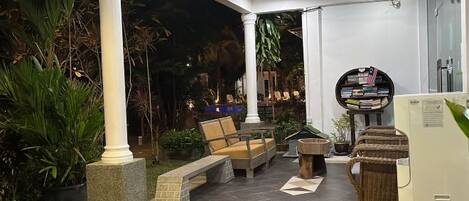 An outdoor seating area with a table and chairs, surrounded by plants and a bookshelf.