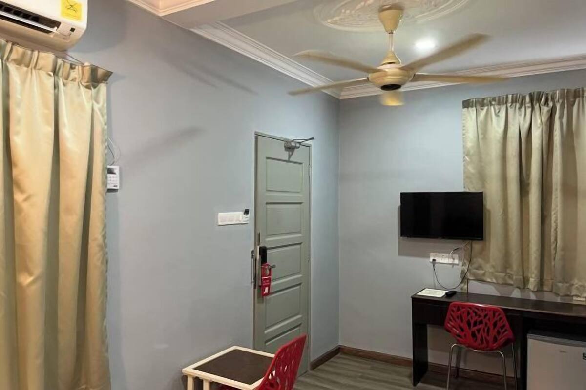 A room with a ceiling fan, a desk with a TV, a chair, and a door.