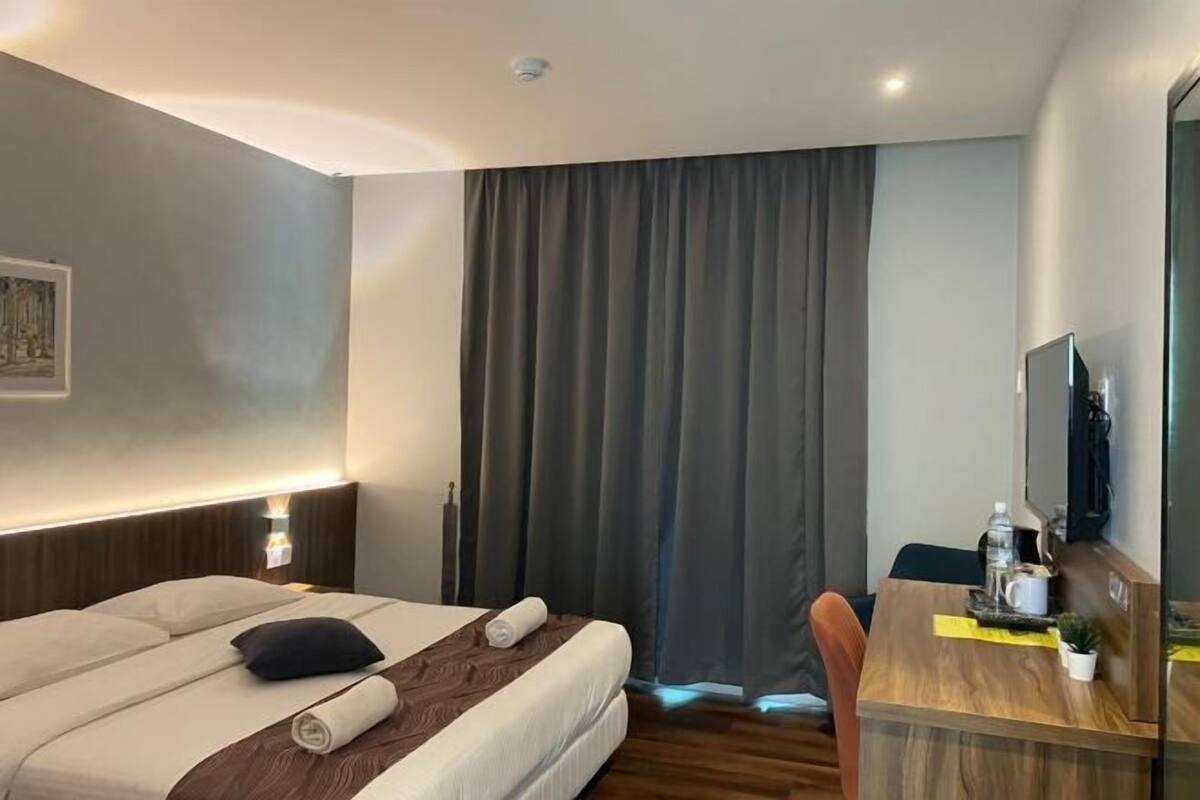 A hotel room with a bed, a desk, a television, and a curtain.