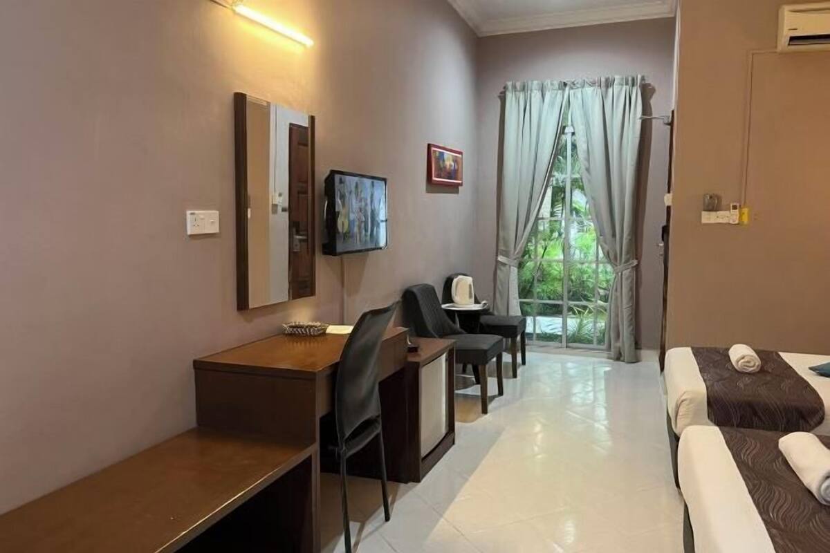 A hotel room with a bed, a desk, a chair, a television, and a window with curtains.