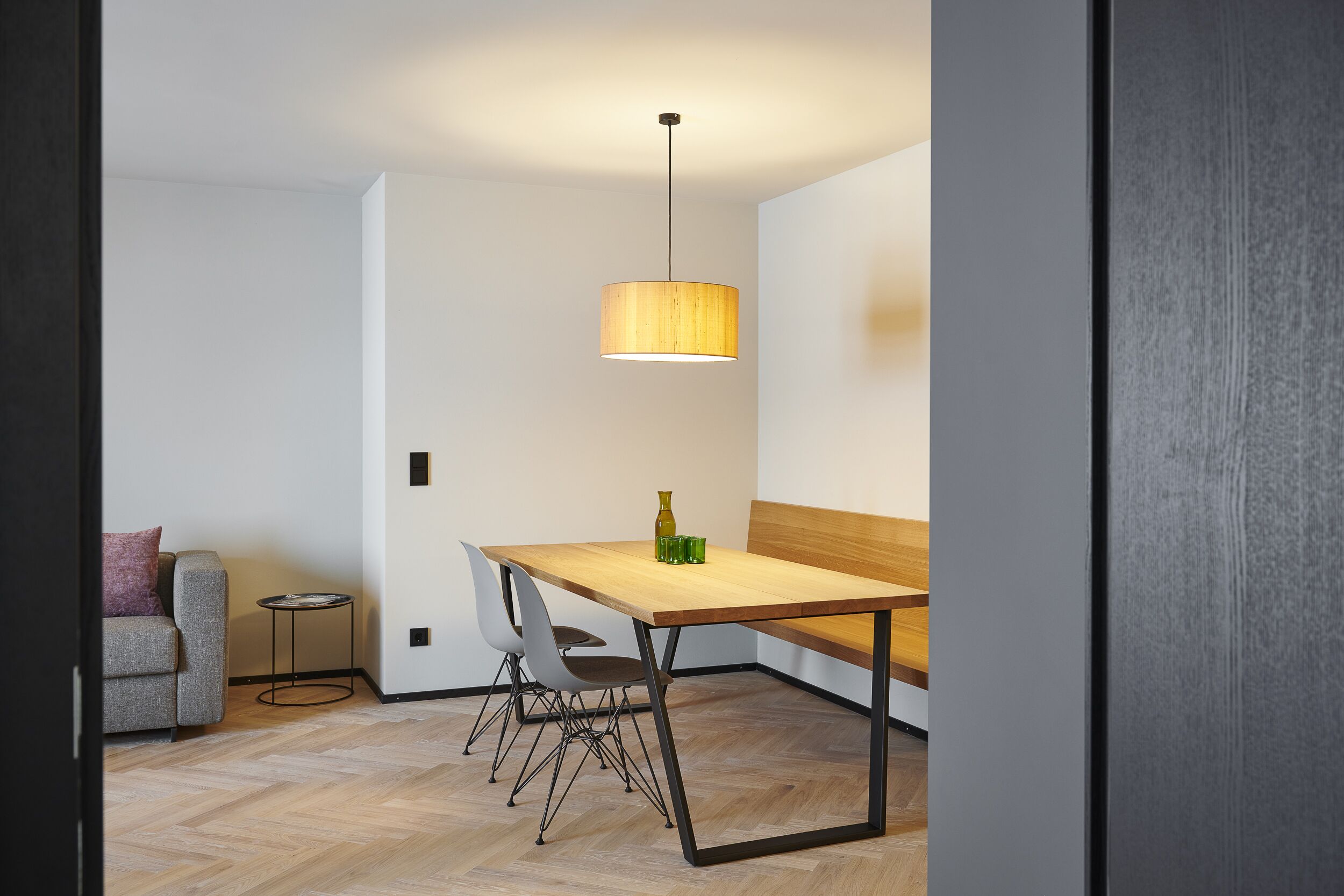 A modern dining area with a wooden table, metal chairs, a bench, and a hanging light fixture.