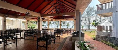 An outdoor covered seating area with tables and chairs, a red roof, and a view of the surrounding landscape.