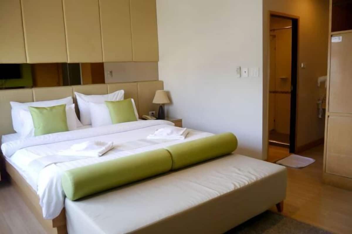 A hotel room with a large bed, a bedside table, a lamp, and a wardrobe.