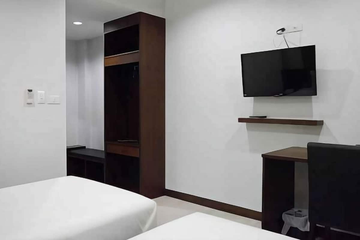 A hotel room with a bed, a TV mounted on the wall, a small table, and a wardrobe.