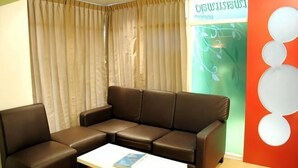 Ein moderner Wartebereich mit einem braunen Ledersofa, einem weißen Couchtisch und einem großen Fenster mit beige farbenen Vorhängen.