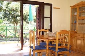 A dining area with wooden chairs and a table, a glass cabinet, and a view of greenery outside.