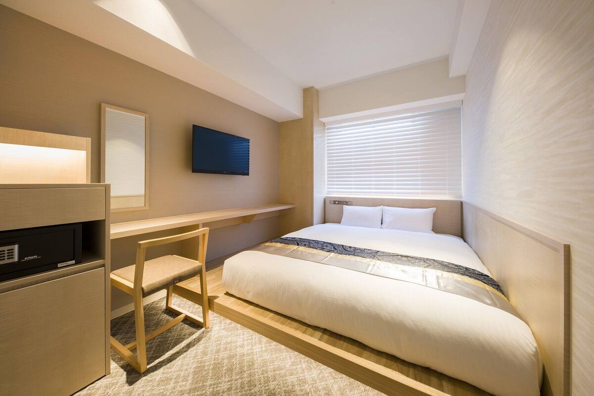 A bedroom with a bed, a desk, and a television.