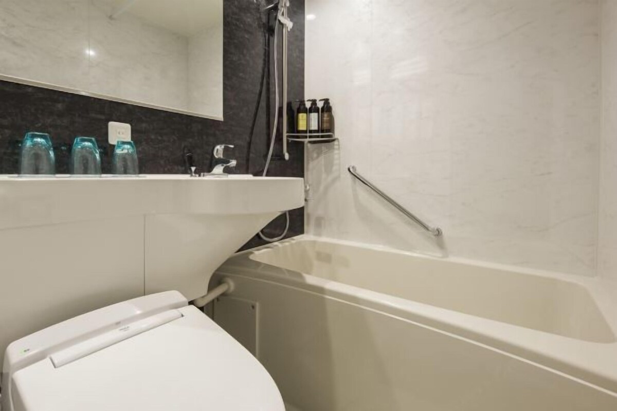 Une salle de bain moderne avec des toilettes blanches, un lavabo doté d’un plan de travail en marbre et une baignoire.