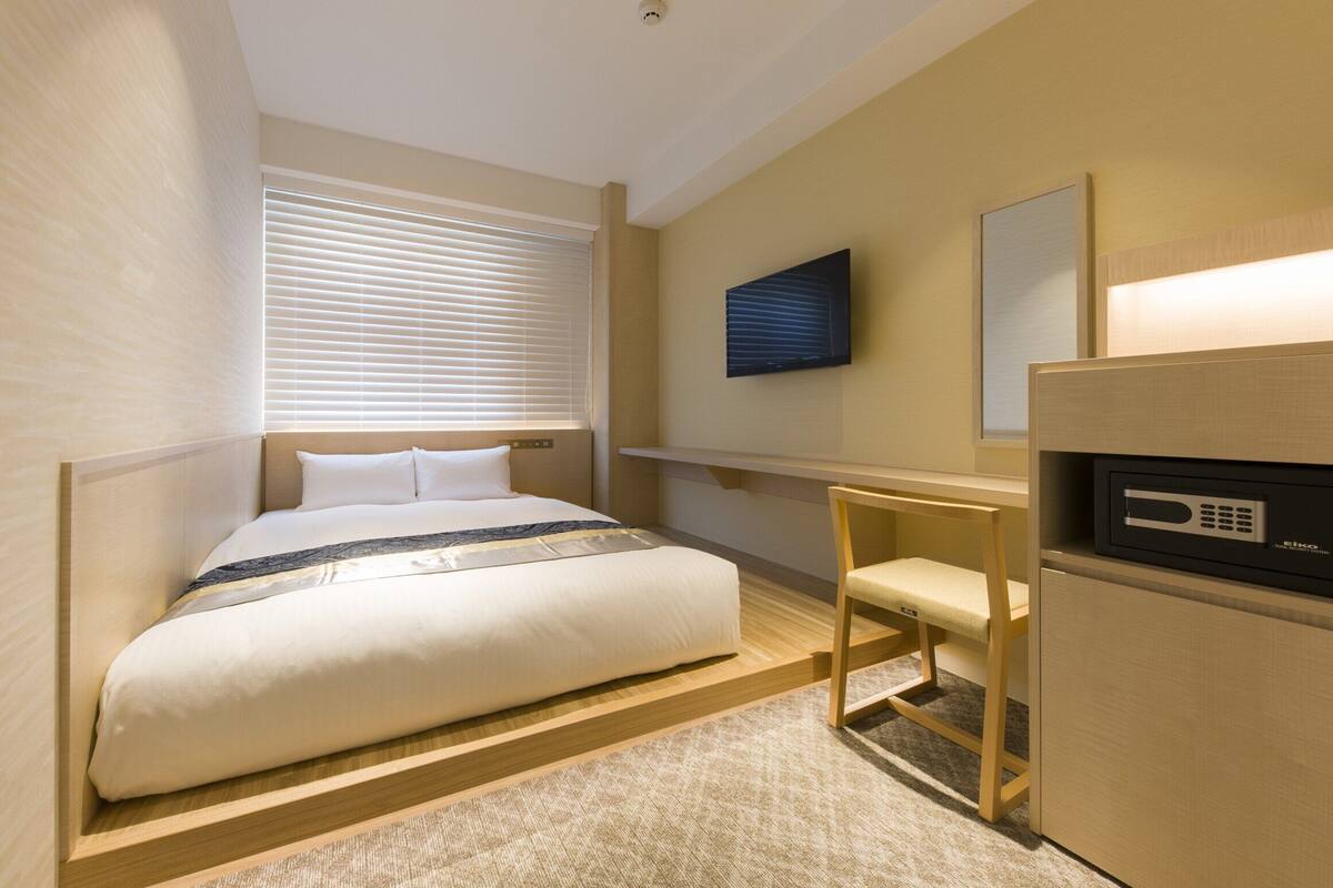 A hotel room with a bed, a desk, a chair, a television, and a minibar.