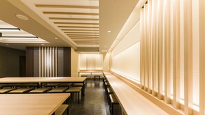 Uma sala de conferências moderna com mesas e bancos longos, iluminação embutida e uma parede de destaque em madeira.