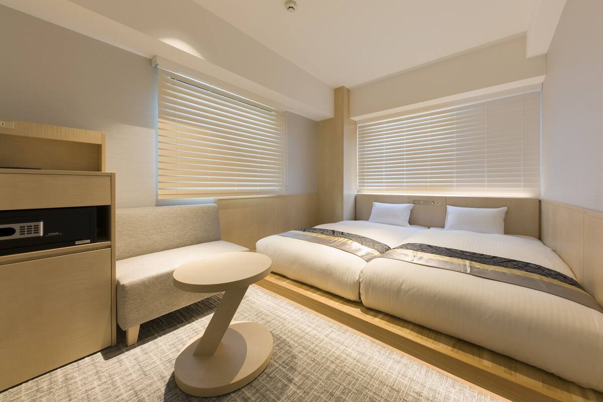 A hotel room with a bed, a small sofa, a round table, and a built-in TV.