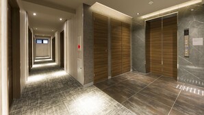 Um corredor moderno de hotel com um longo vão, portas de madeira e uma parede de mármore.