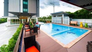 A modern building with a swimming pool, outdoor seating, and a covered area. - GT Residence Hotel (Buriram)