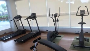 A gym with treadmills, an elliptical, a bench, and a rowing machine. - GT Residence Hotel (Buriram)