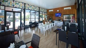 A spacious indoor area with tables and chairs, a television, and a Coca-Cola refrigerator. - GT Residence Hotel (Buriram)