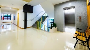A modern lobby with a staircase, a bench, and an elevator. - GT Residence Hotel (Buriram)