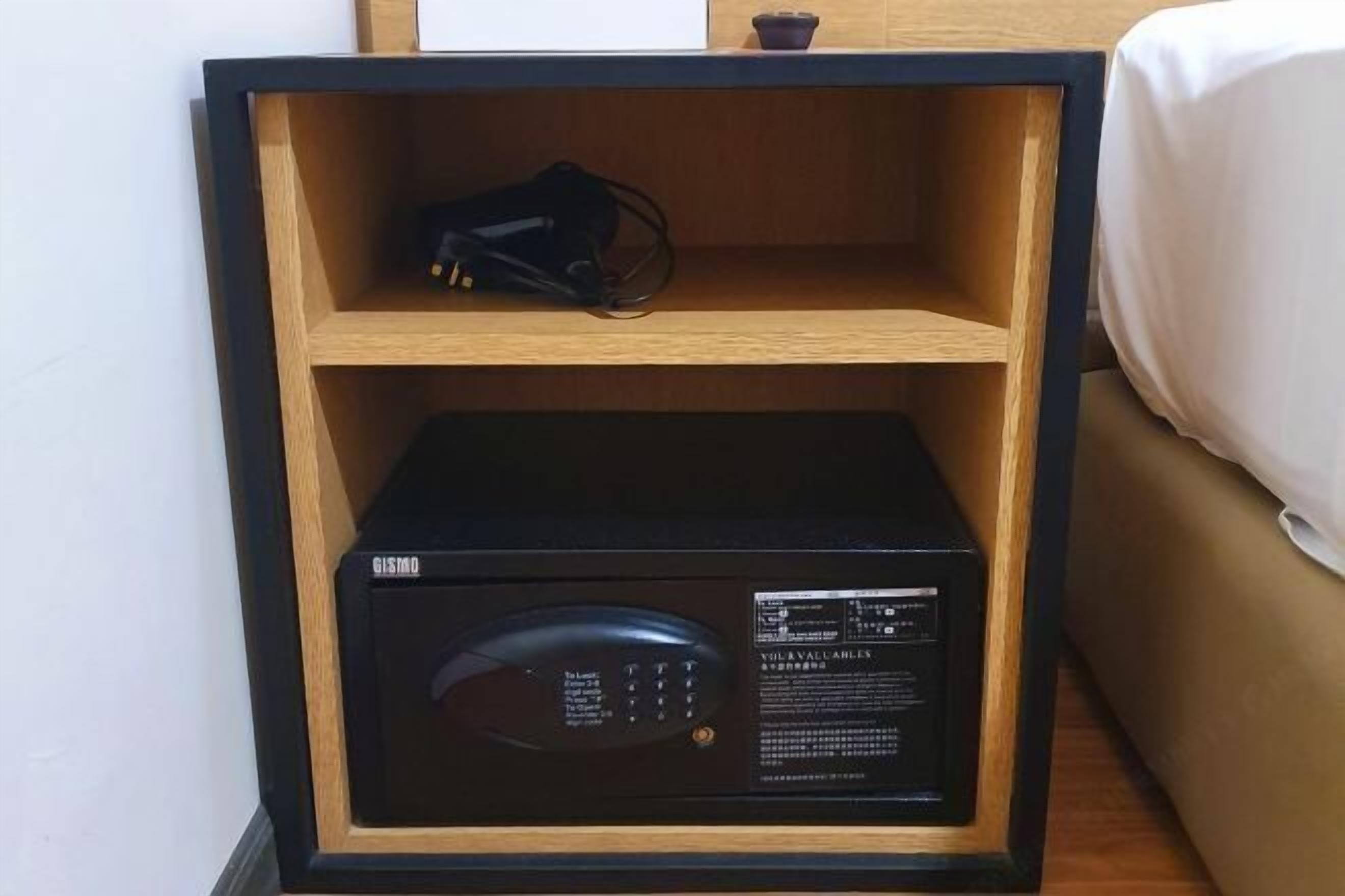 A black microwave in a wooden cabinet with a control panel and a small black object on the top shelf.