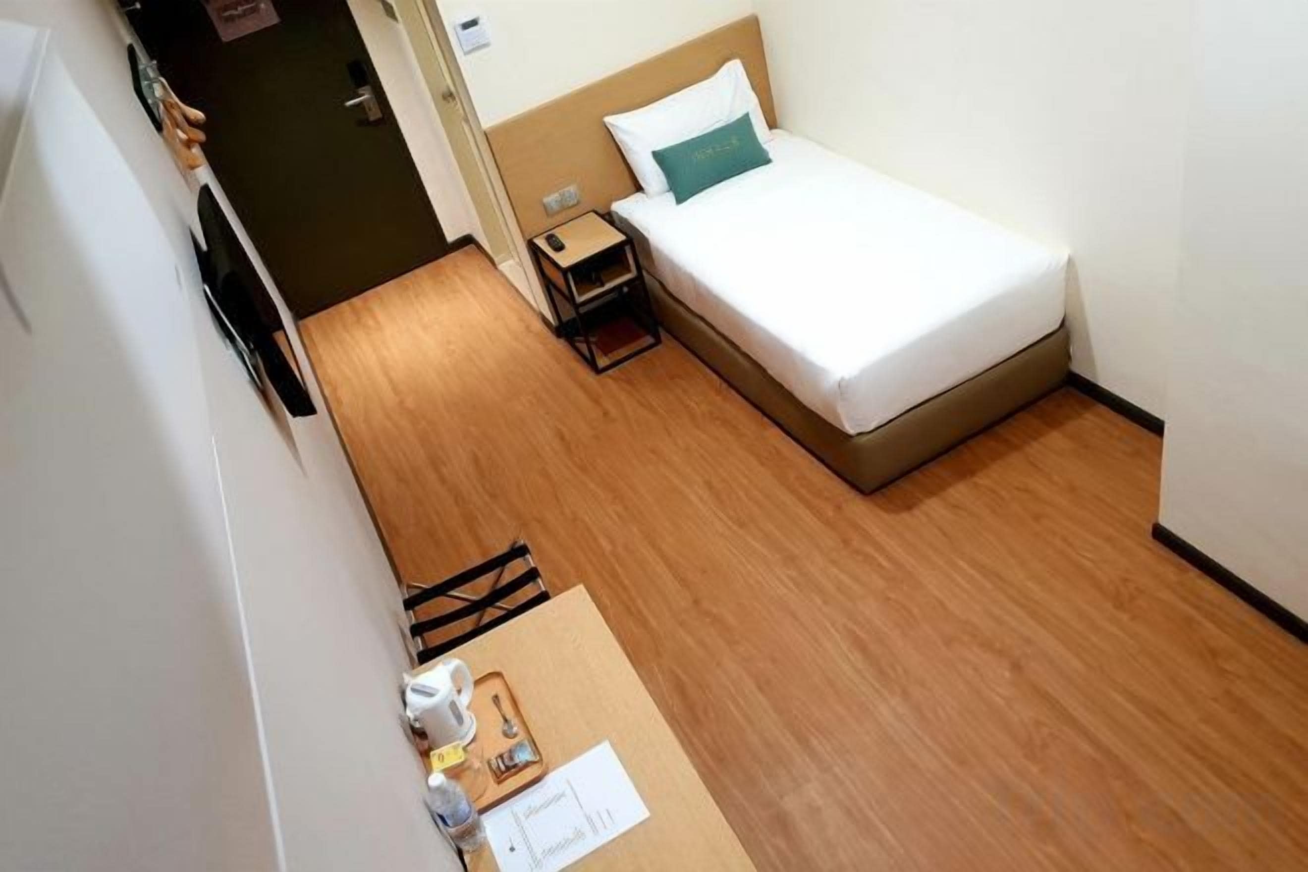A small hotel room with a single bed, a bedside table, and a wooden floor.