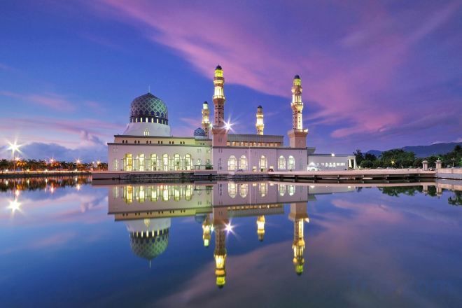 Een moskee met een grote koepel en meerdere minaretten, weerspiegeld in een kalm waterlichaam.