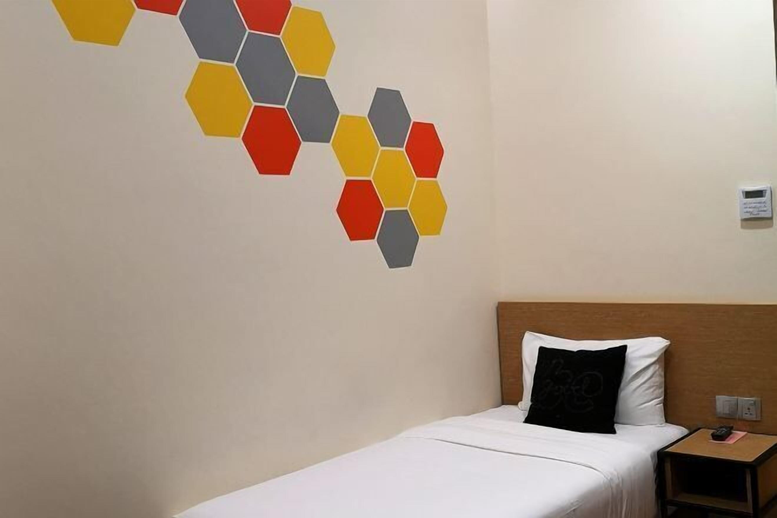A hotel room with a bed, a nightstand, and a wall decoration of hexagonal shapes in red, yellow, and gray.
