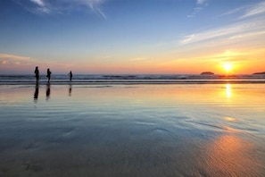 A beach scene with a sunset, calm water, and silhouettes of people. - Qlio Hotel (Kota Kinabalu)
