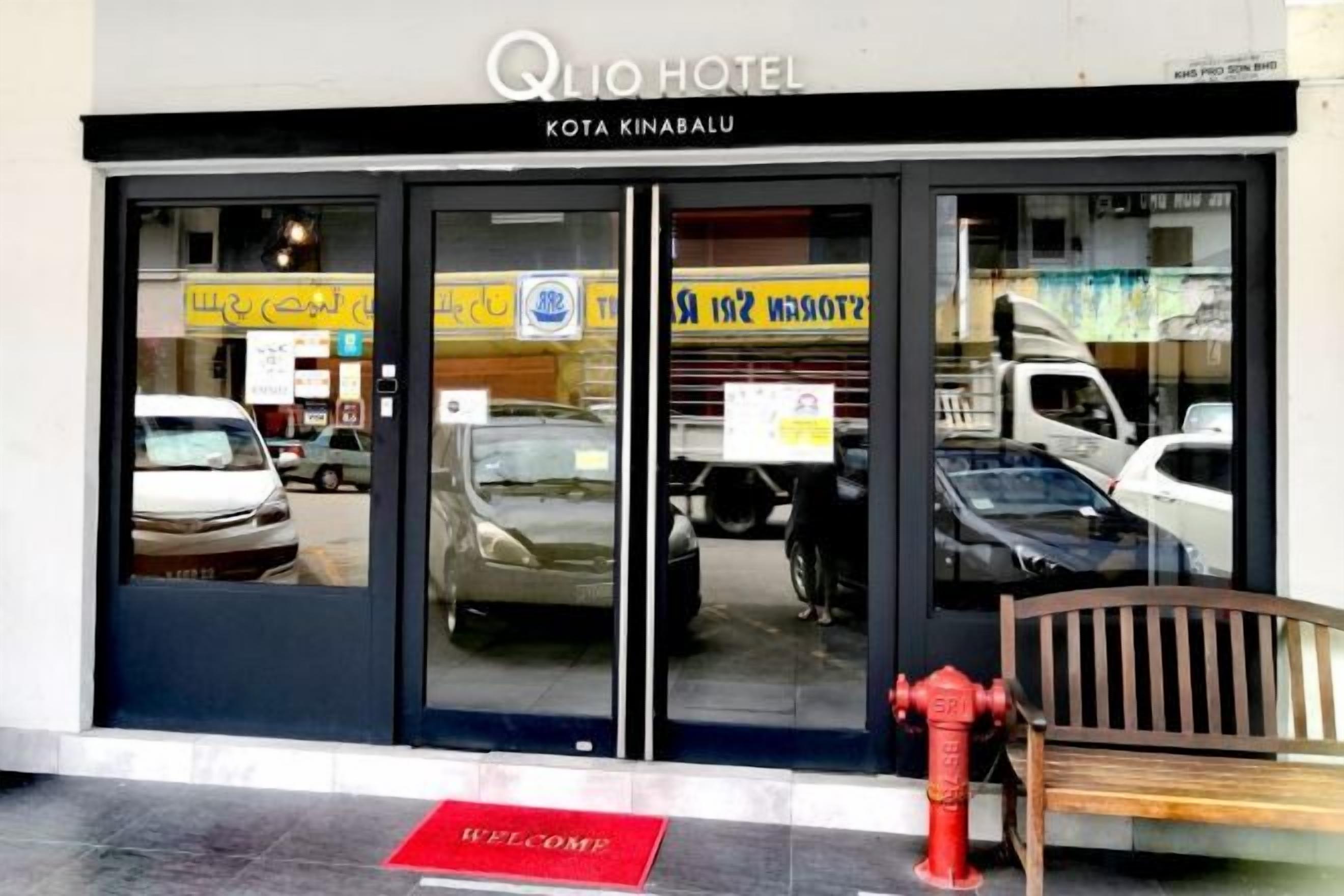 The entrance to Qlio Hotel Kota Kinabalu with a red fire hydrant and a wooden bench outside.