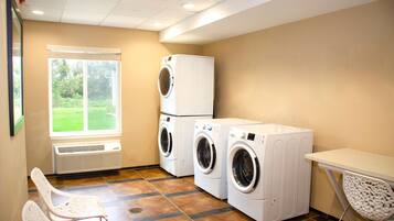 A laundry room with two stacked washing machines, a table, and a chair.