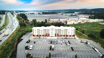 Un hôtel à plusieurs étages, doté d’un parking à l’avant, entouré de verdure et bordé par une autoroute.