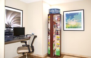 Un bureau avec un ordinateur, une imprimante et une chaise, un présentoir à magazines et deux tableaux encadrés accrochés au mur.