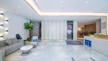 A modern hotel lobby with a reception desk, seating area, and a plant.