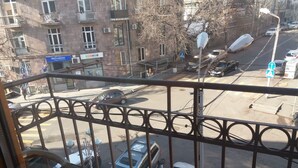 Vista de la calle desde un balcón con barandilla de metal, coches estacionados y edificios al fondo.