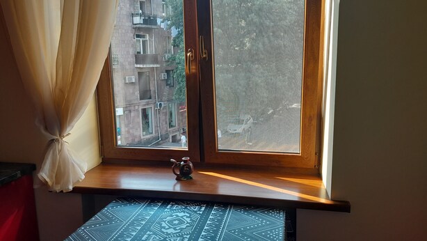 Una ventana con vistas a un edificio, una cortina y una pequeña mesa con mantel estampado.