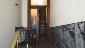 A hallway with a marble wall, a wooden door with a glass panel, and a staircase.