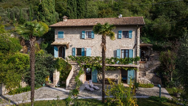 Una casa de piedra con techo de tejas, múltiples ventanas con contraventanas y una pequeña escalera que lleva a la entrada.