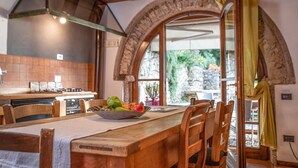 Una cocina rústica con una mesa de madera, sillas y un bol de fruta.