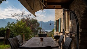 Un patio al aire libre con una mesa y sillas, vistas a montañas y un muro de piedra.