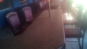 A long, rectangular dining table with chairs on both sides, a tiled floor, and a window with blinds. - Jaws Palace Umoja (Nairobi)