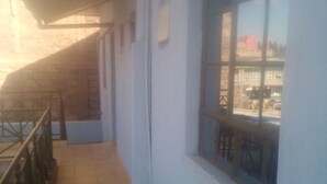 A corridor with a tiled floor, a window with a view of the outside, and a metal railing on the left. - Jaws Palace Umoja (Nairobi)