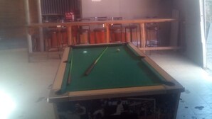 A pool table in a room with a bar area and several stools. - Jaws Palace Umoja (Nairobi)