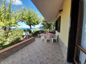 A patio with a table and chairs, a view of the sea, and a garden area with trees and plants.