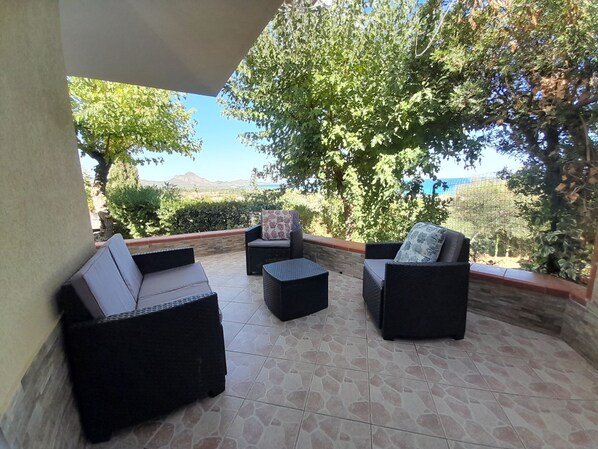 A covered patio with outdoor furniture, a stone floor, and a view of the sea and mountains.