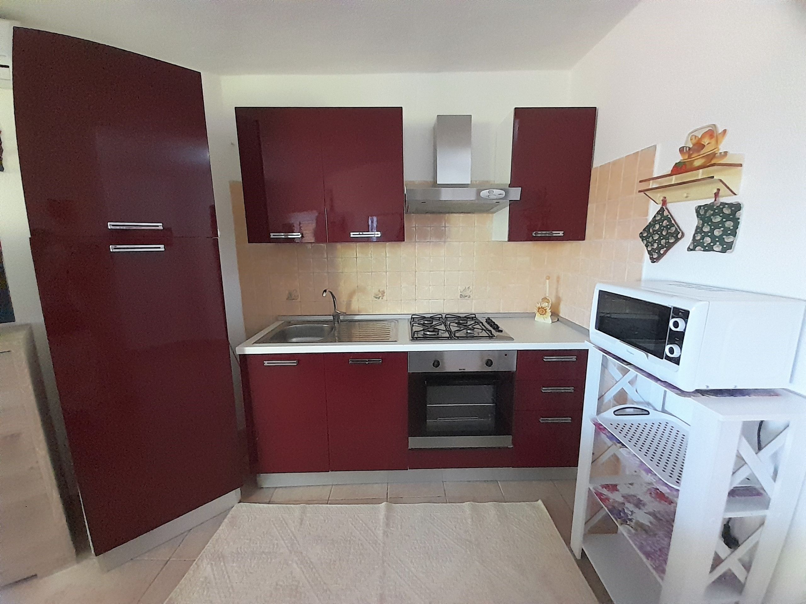 A compact kitchen with red cabinets, a gas stove, a microwave, and a small oven.