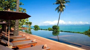 An infinity pool with lounge chairs and a palm tree, overlooking a clear blue sea. - Saree Samui (Koh Samui)